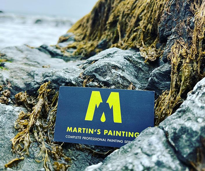 Business card on rocky, seaweed-covered surface.