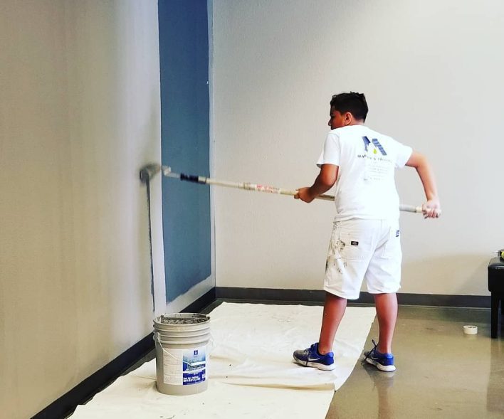 Person painting wall with roller and bucket.